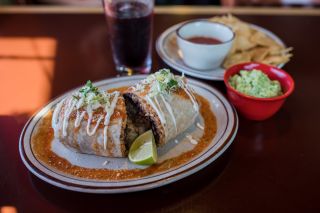 A burrito, sliced in half, on a plate with chips and salsa on the side