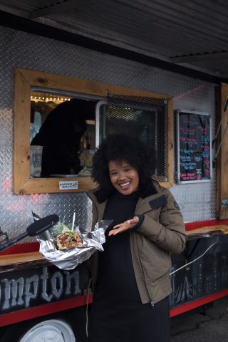 A woman holds food in front of a mobile food cart