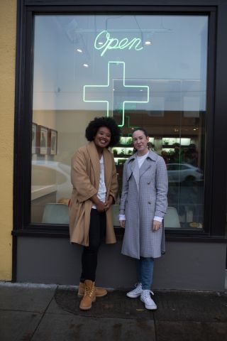 two women stand in front of a legal cannabis dispensary