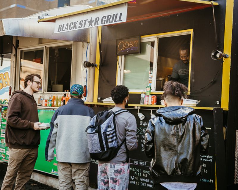 People lined up at a food cart serving African meals