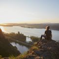 person sits on top of a rock overlooking the Columbia River as the sun sets