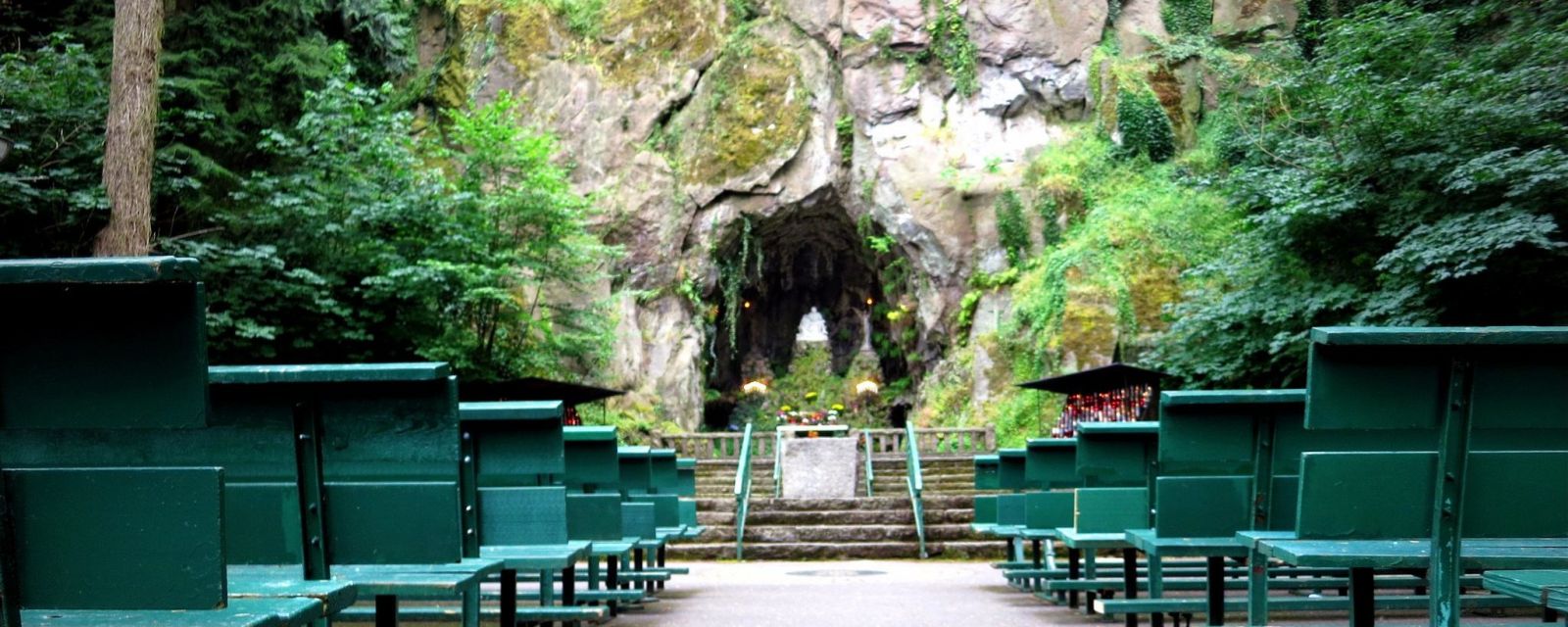 rows of benches face a rock wall and tunnel surrounded by moss, trees