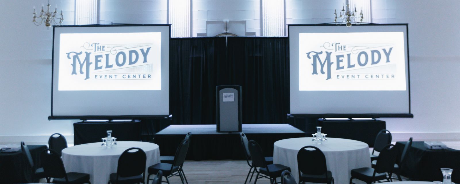 tables and chairs set for an event with two screens and a podium in front at Melody Event Space