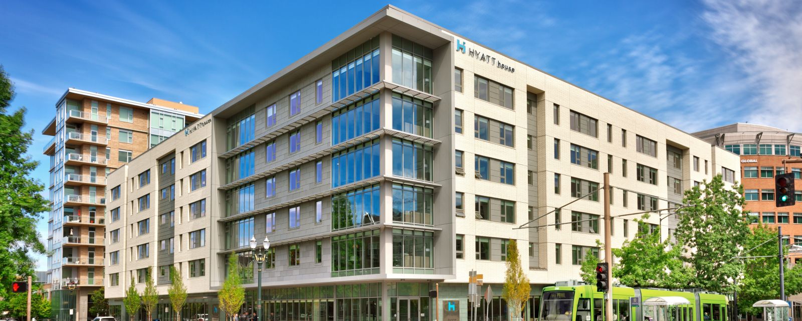 Exterior view of Hyatt House Hotel with six stories and a green max train running in front