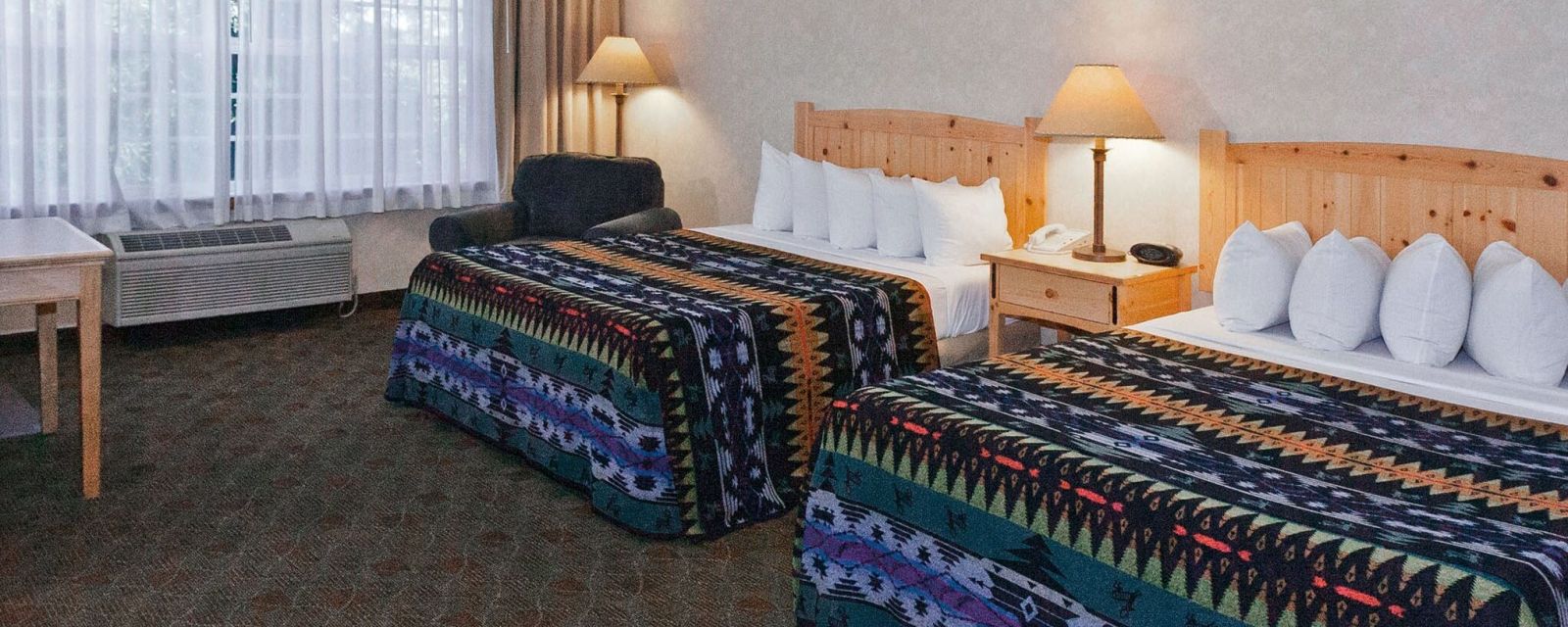 two queen sized beds covered with colorful blankets with geometric patterns in a hotel room