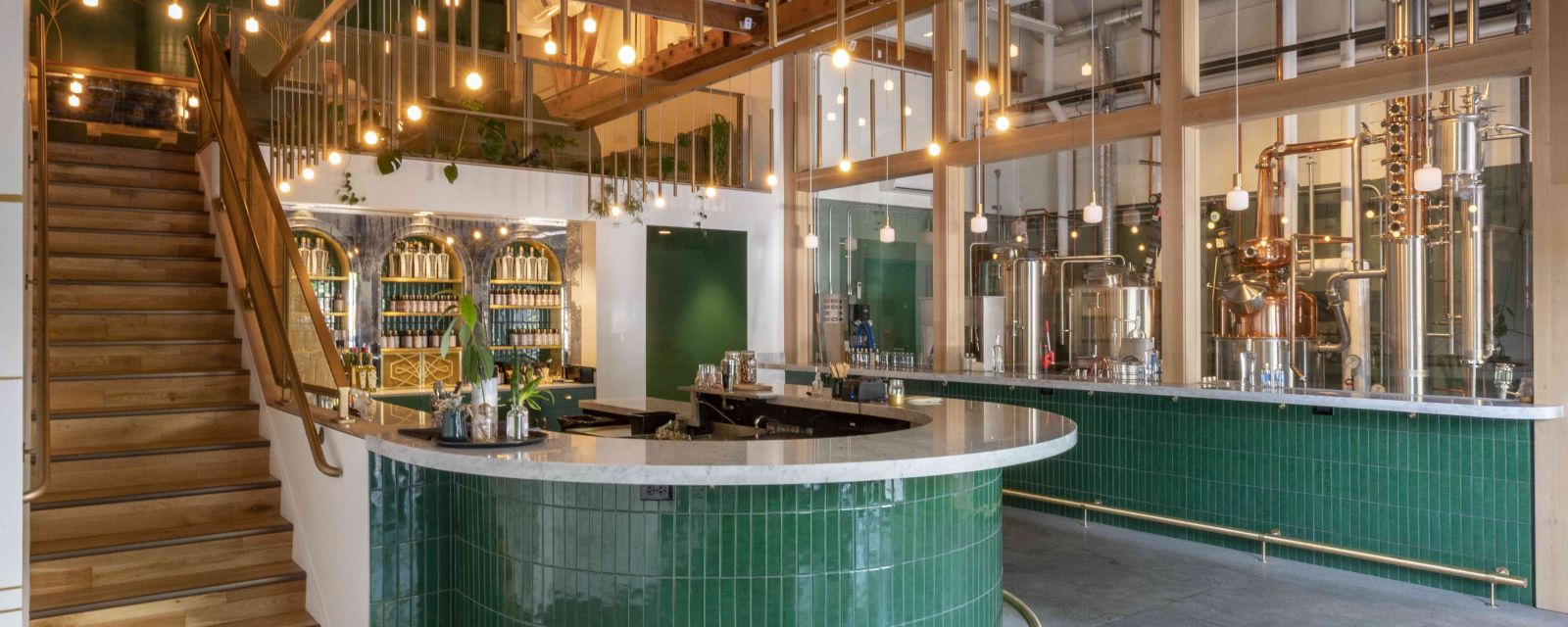 A rounded bar top featuring a distillery to the right and a staircase to the left leading to more seating.