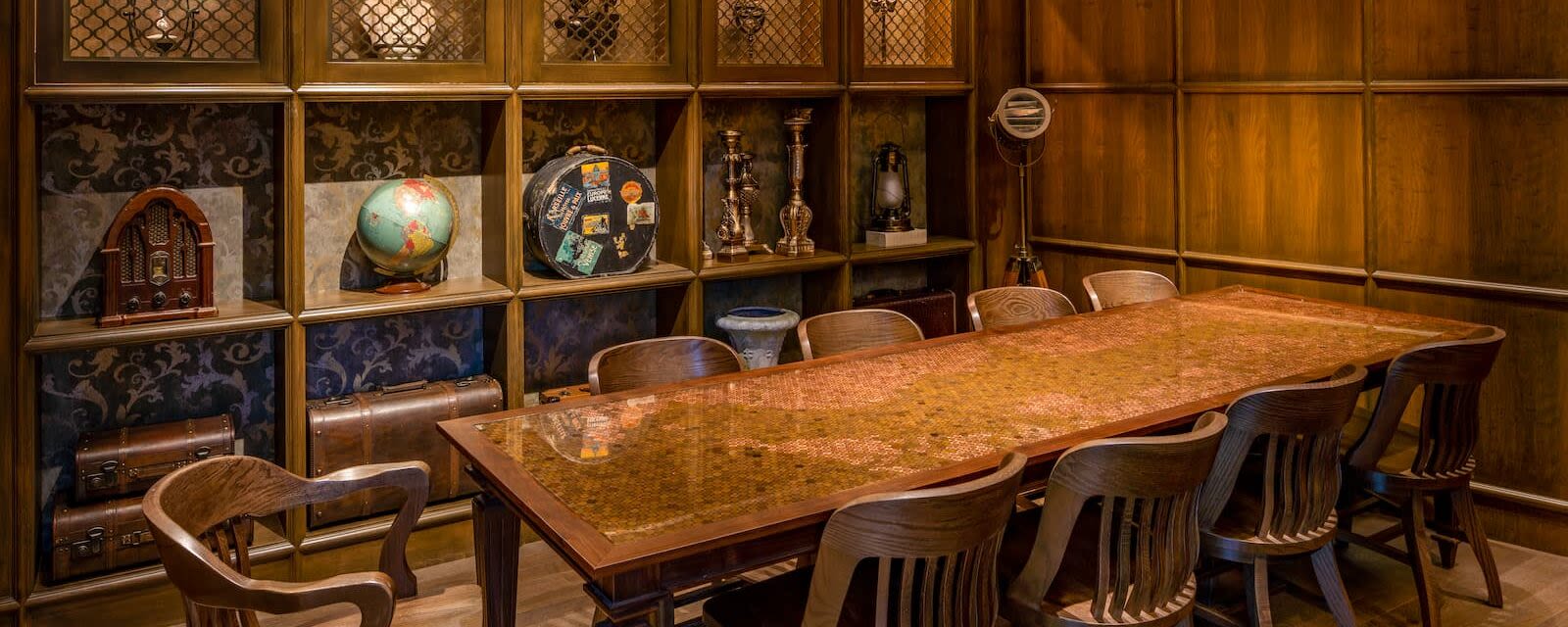 a sturdy wooden table surrounded by chairs with a shelf of curios in the background