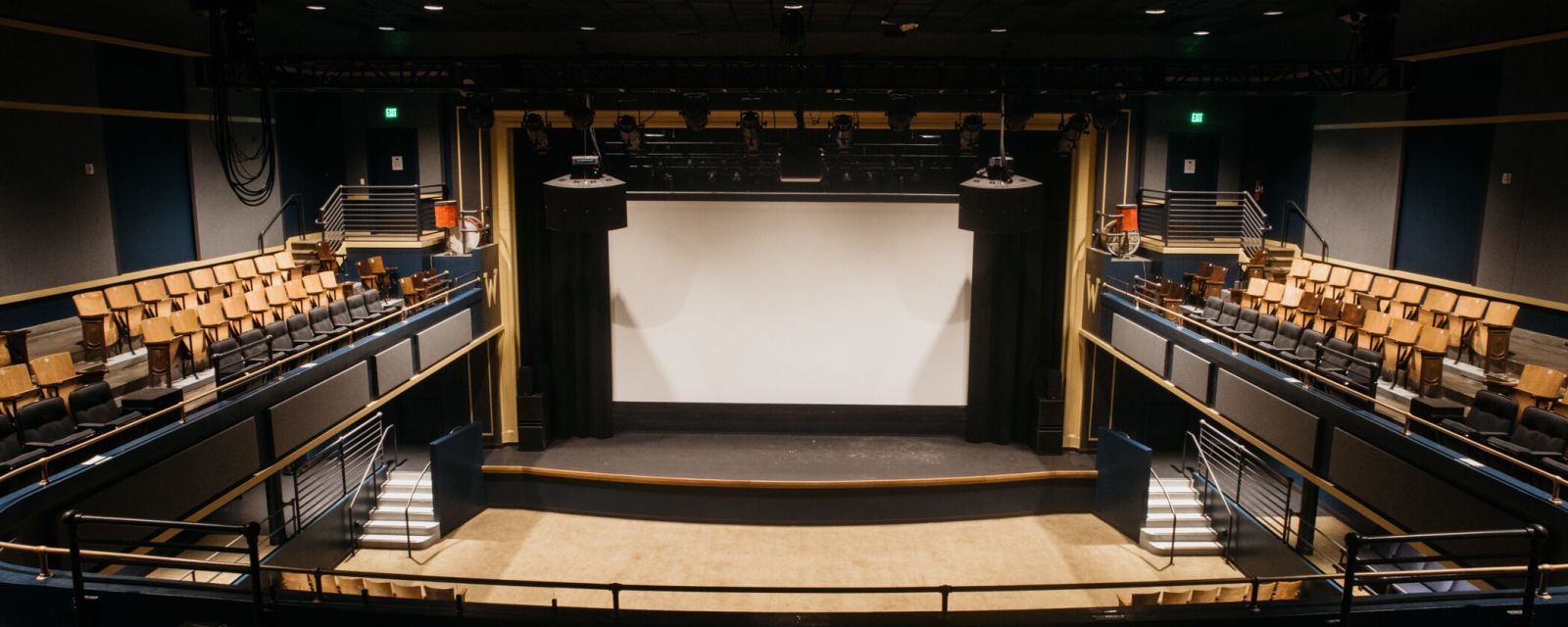 an empty auditorium with two-level seating, large speakers, a stage and a projection screen