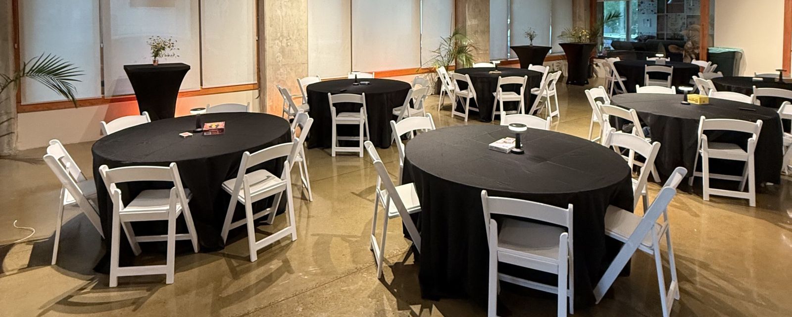 An industrial event venue with round tables draped in black tablecloths and white chairs.