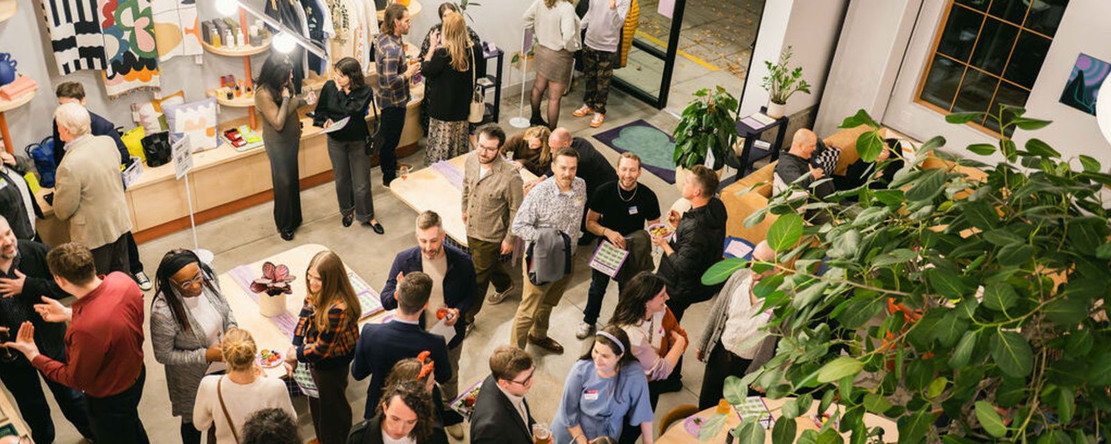 A view looking down into a large room full of people. The room is open and clean, with some clothing wares displayed on the wall and a large tree in the center of the room.