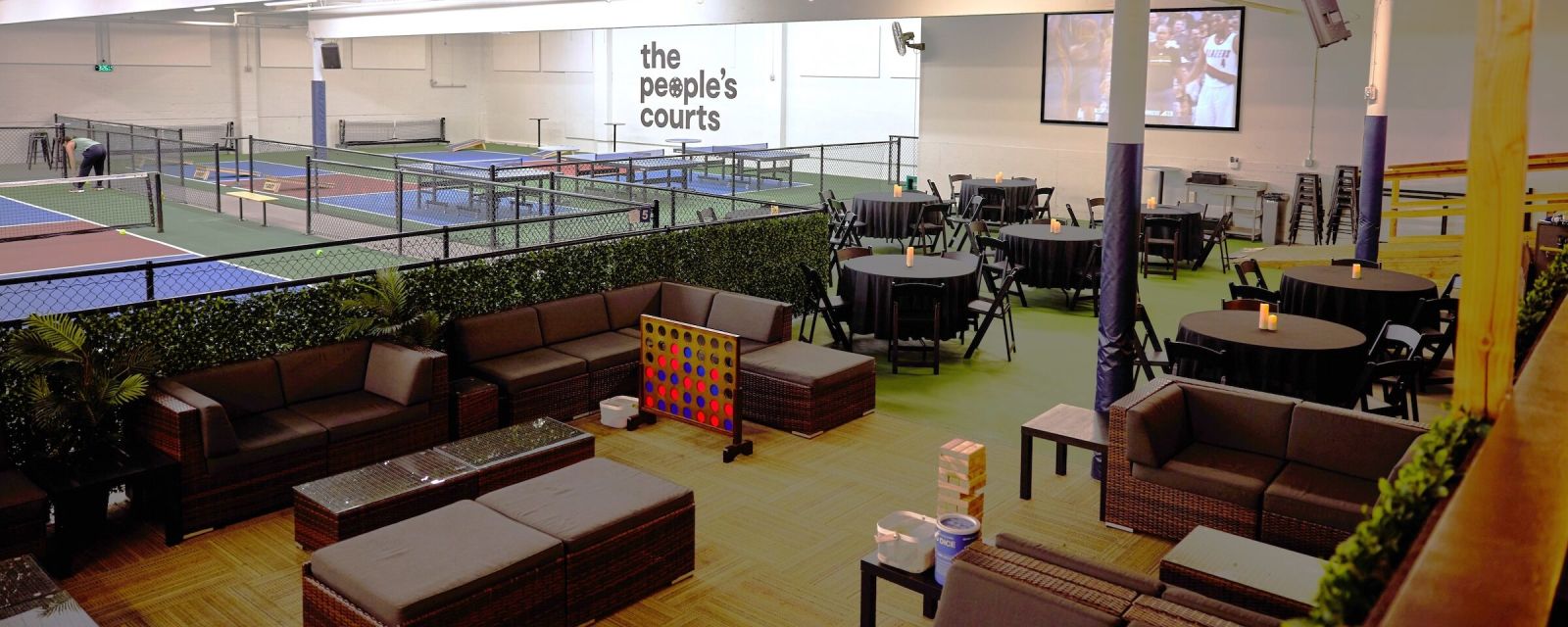 A series of tables and couches in the foreground pair with pickleball courts in the background.