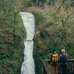 Two people view a waterfall from a wood deck