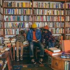 Three people sit and read a book at Mother Foucault\'s bookstore in front of a wall of books.