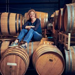 A woman in long-sleeved t-shirt, jeans and sneakers sits on top of large wooden barrels