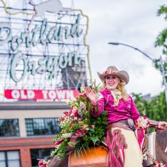 woman riding a horse adorned with roses waves during a parade in downtown Portland