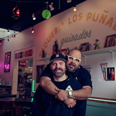 two people hugging inside of a restaurant with art and the restaurant name on the wall behind them