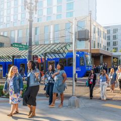 Group of people walking across the street with light rail in the background
