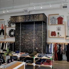 clothing on racks and folded on tables and large display with handwritten words