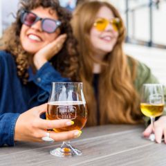 two women in sunglasses enjoy glasses of cider at a patio table