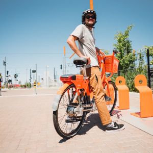 A person standing over an orange bike next to bike stands