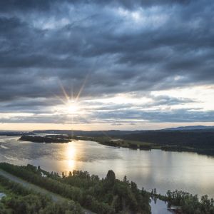 The sun breaks through clouds above a wide river