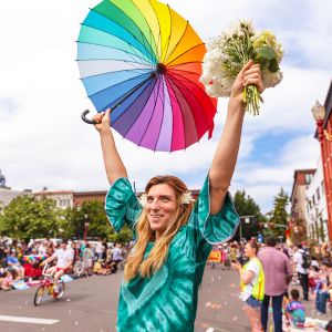 person holding up bouquet of flowers and rainbow flag during parade in a street parade