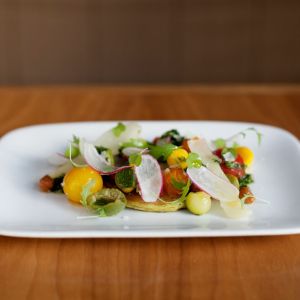 a white platter of delicately prepared, colorful vegetables on a wooden table