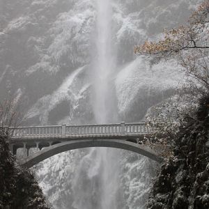 a towering waterfall behind a stone bridge surrounded by snow and ice