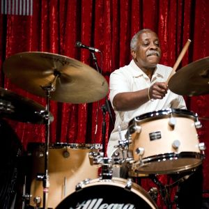 a man playing drums on stage in front of a red curtain