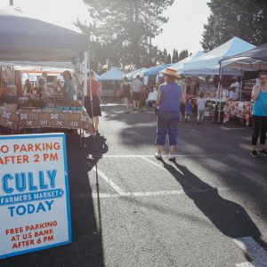 a parking lot filled with farmers market vendors, and a sign for the cully farmers market