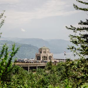 the vista house is in the distance, framed by brush and tree branches on three sides in the foreground