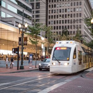 A light rail train passes in front of a modern, glass-encased retail store