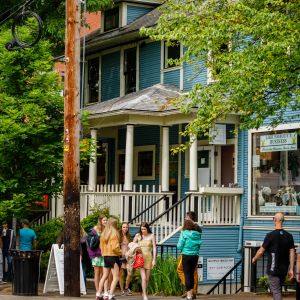 groups of people and couples walking on busy tree-lined street filled with storefronts in old Victorian homes