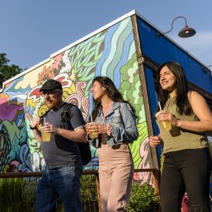 walking toward the sun, three people pass a colorful mural painted on the side of a building