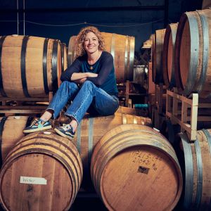 A woman in long-sleeved t-shirt, jeans and sneakers sits on top of large wooden barrels