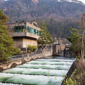 fish ladder with utilitarian building off to the side in front of a hillside with waterfalls and a winter forest