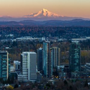 sunset catches a large snow-capped peak that towers behind an expansive city landscape
