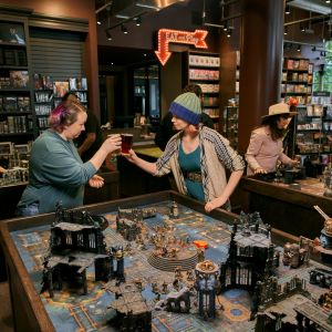 Two friends clinking glasses over a large tabletop board game.