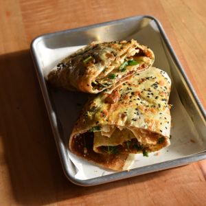 One serving of Jianbing, cut in two, rests in a silver lunch tray on a wooden table.