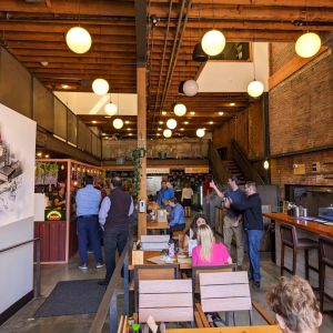 people in line to order food, while others sit at a bar or tables in a hip food hall