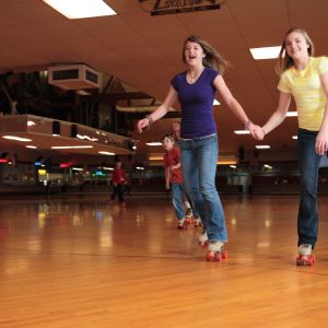 two people smile while holding hands and skating across a classic wooden roller rink