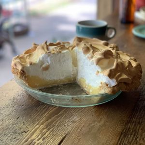 a tall lemon meringue pie with a couple of slices missing sitting in a glass pie dish