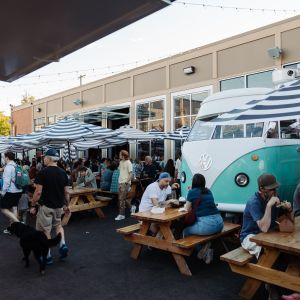 many people sitting at outdoor tables eating and mingling at a busy food cart pod