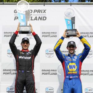 two race car drivers hold up their winning trophies