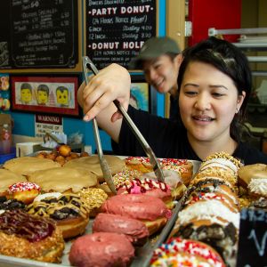 person using tongs to select a doughnut from a tray