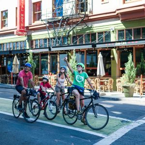 family on bikes stop in green bike lane, one pointing up with building towering behind them in cityscape