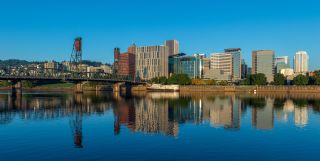 calm river water reflects the buildings in a downtown area that are catching the sunrise on a clear day