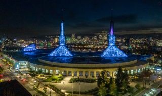 a vast building with two blue spires at night with the bright city skyline in the background