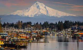 colorful boathouses sit atop the still water beneath the towering white-capped mountain