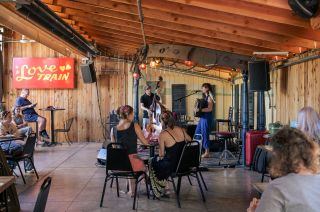 covered outdoor patio with stage and a band singing and playing accordion and upright bass for people seated at tables